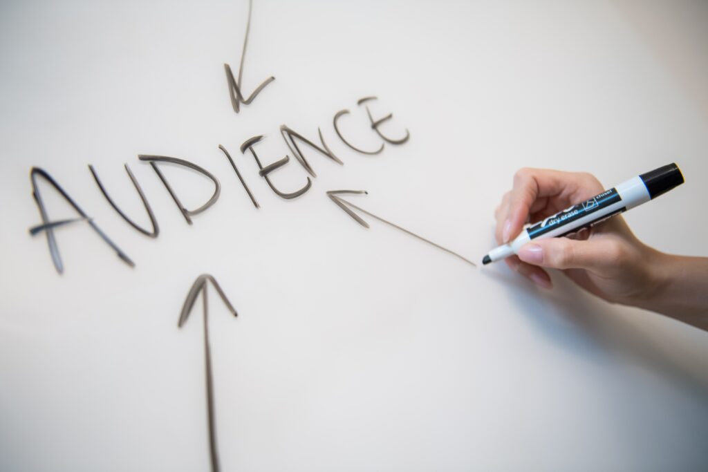 person writing the word audience on whiteboard